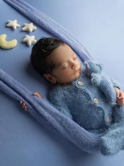 A different angle of the swing pose, showing the baby peacefully cuddling a small blue teddy bear while he dreams.