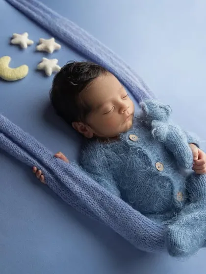 A different angle of the swing pose, showing the baby peacefully cuddling a small blue teddy bear while he dreams.
