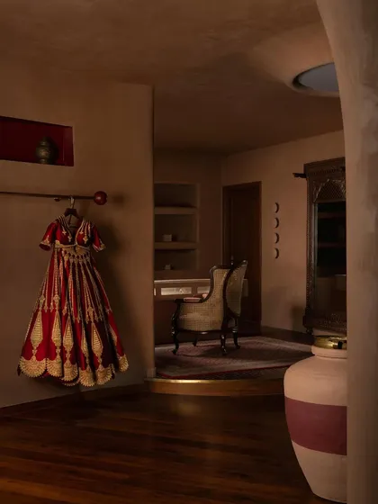 A bridal lehenga hangs in a dedicated niche, the rich red of the garment complementing the warm, earthy tones of the walls.