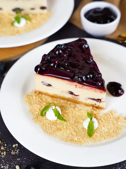 A slice of blueberry cheesecake with a generous topping of glossy blueberry compote. The bright, clean lighting and simple presentation make the dessert look fresh and irresistible.