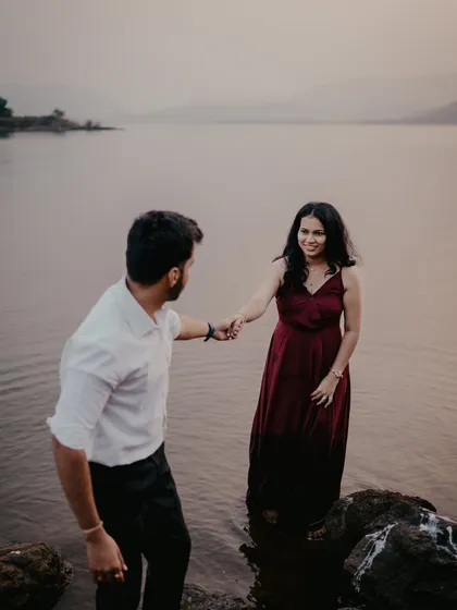A playful moment during a lakeside pre-wedding shoot near Pune. The groom leads the bride into the water, creating a spontaneous and romantic scene against the dusky landscape.