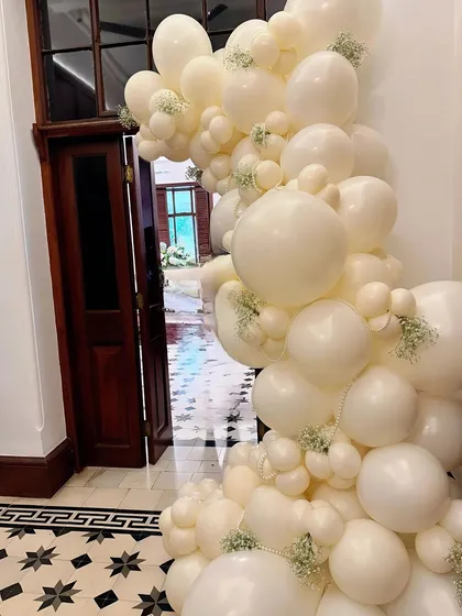 An ivory balloon arch decorated with baby's breath and pearls, making for a sophisticated and celebratory entrance.