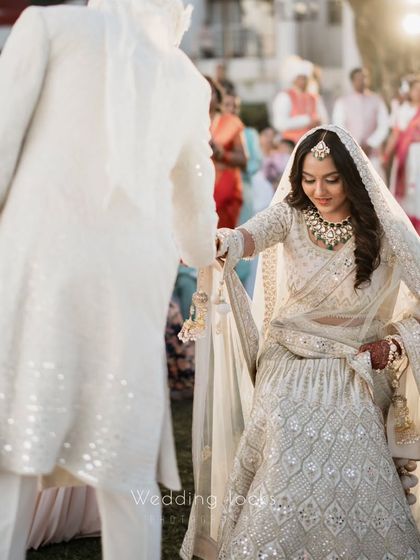 A candid shot of the groom leading his bride, capturing the movement of her lehenga and the natural interaction between them.