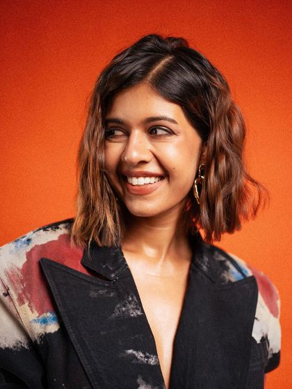 A bright and engaging portrait of Sejal Kumar. Her genuine smile and the vibrant background create a warm and positive image, perfect for a lifestyle-oriented brand campaign.