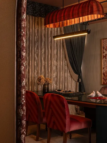 A detail of the client interaction zone, focusing on the custom red chairs and the layered drapery. The light from the bespoke chandelier catches the texture of the curtains, adding warmth and drama to the space.
