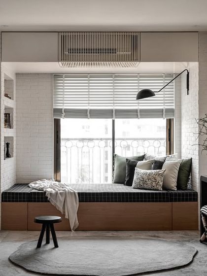 This versatile space serves as both a living area and a guest room. The cozy daybed with black plaid upholstery is set against a white brick wall with built-in book niches, creating a perfect reading nook that is both stylish and functional.