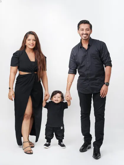 A chic family photo where parents and their young son are dressed in matching black outfits, holding hands for a full-length portrait.