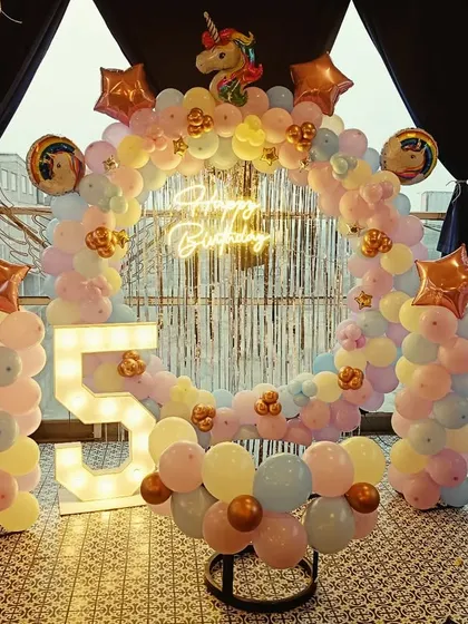 A magical unicorn-themed 5th birthday party. This outdoor setup features a full ring arch with pastel rainbow balloons, a unicorn foil balloon, a neon sign, and a light-up number '5'.