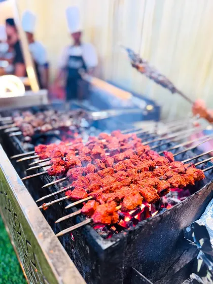 Vibrant red Chicken Tikka and darker Khiri Kaleji kebabs cook side-by-side on the grill, offering guests a variety of flavors.