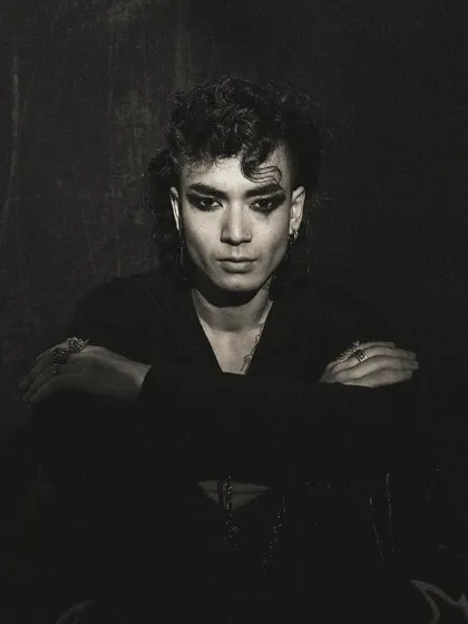 A dark and moody portrait from a men's editorial. The low-key lighting and the model's crossed arms create a feeling of introspection and intensity.