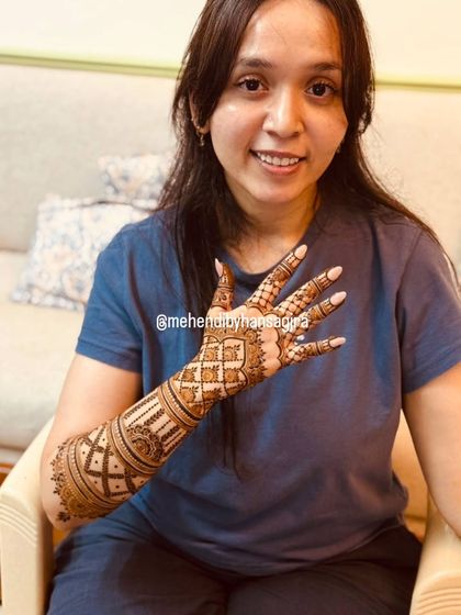 A happy bride showing off her minimal yet elegant back-of-hand design. Her relaxed smile and casual attire show that mehendi is a beautiful part of the entire wedding journey.