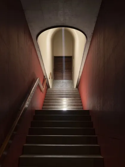 A dramatic, light-filled staircase at the Vismaya museum. A narrow slit of light from a skylight above illuminates the path, creating a powerful, almost spiritual transition between gallery levels.