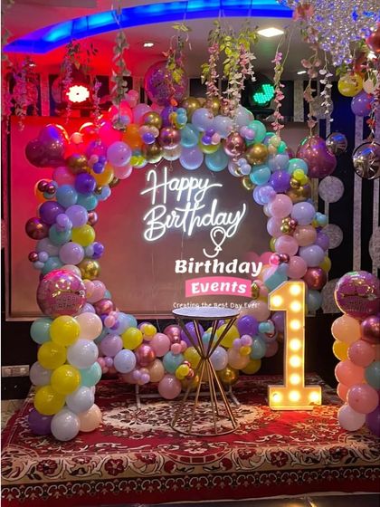 A colorful and fun first birthday party. The light-up number "1" stands next to a rainbow pastel balloon arch and neon sign.