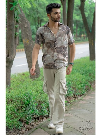 A full-length outdoor shot showcasing a casual, contemporary men's outfit. The natural, leafy background provides a great contrast to the stylish streetwear look.