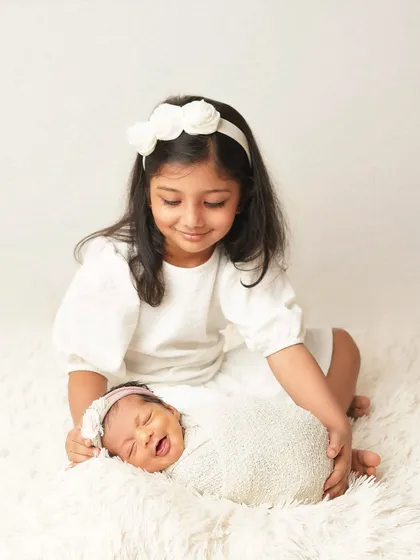 A big sister gently holds her newborn sibling, who is making a funny face. This candid moment captures the real, unscripted nature of sibling love.