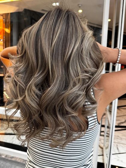 This shot captures the full, voluminous look of the ash blond balayage, styled in beautiful waves.