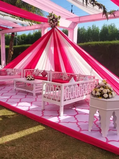 An inviting and chic lounge setup for a Mehndi function. The pink and white color scheme is carried through the drapes and furniture, creating a perfect space for guests to relax and mingle.