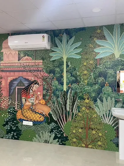 This large-scale Pichwai-style mural depicts a serene scene in a lush garden. The traditional art form and detailed imagery add a sense of heritage and storytelling to this spacious room.