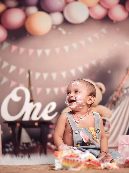 The pure joy of a first birthday cake smash. This little one's happy, messy face says it all, surrounded by a fun setup of balloons and presents.