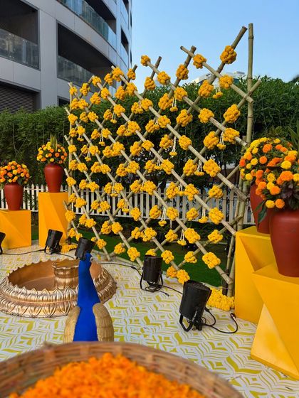 An angled view of the outdoor Haldi setup, showing the arrangement of props like the peacock figure, terracotta vases, and yellow pedestals that frame the main stage area.