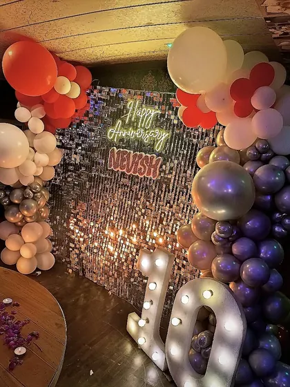 Celebrate a decade of love with a glamorous party setup. This 10th-anniversary decor features a shimmering silver sequin wall, a personalized neon sign, light-up marquee numbers, and a stylish balloon arrangement.