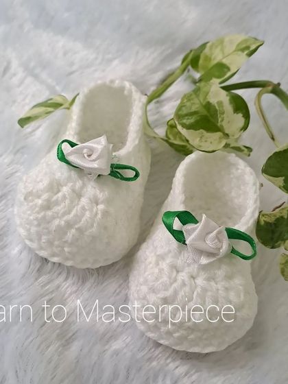 Another look at the white satin rose booties, showing their clean design and soft texture, made from baby-safe acrylic yarn.