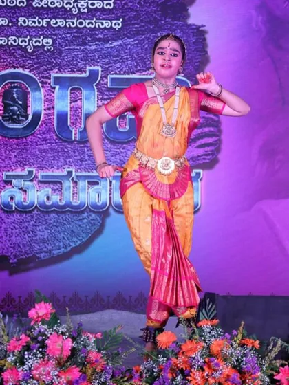 A classical dancer performs on a flower-adorned stage. I make sure to capture the full context of the performance, including the stage design.