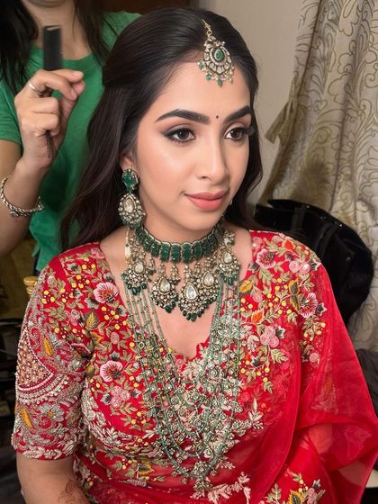 A gorgeous reception look. The soft smokey eye and glowing skin are paired with a beautiful red lehenga and emerald jewelry for a classic, elegant finish.