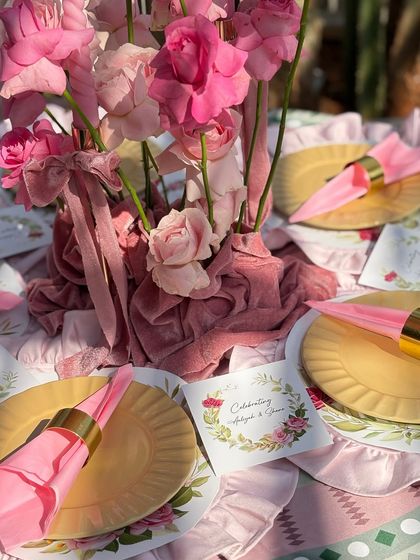 A close-up of the table setting, highlighting the rich textures. A centerpiece of pink roses in a velvet-wrapped vase is paired with custom stationery and bright pink napkins held by gold rings.