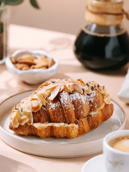 A close-up of the almond croissant, highlighting the flaky layers and almond topping. This detailed shot is designed to make the viewer's mouth water.