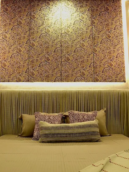 A luxurious bedroom design where lighting and texture take center stage. The custom bed features a pleated fabric headboard, flanked by hanging pendant lights that create a warm, intimate glow. The textured wallpaper behind the bed adds another layer of depth and sophistication.