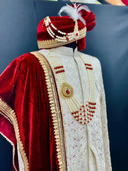 A closer look at the accessories that complete the groom's attire. The velvet turban, pearl and ruby necklace, and embroidered dupatta are all styled to perfectly match the sherwani.