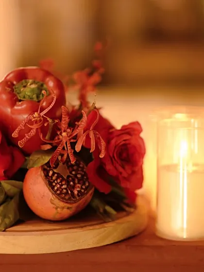 A close-up of a centerpiece from the monochromatic red dinner, featuring a red bell pepper, a pomegranate, and red roses, all illuminated by the soft glow of candles.
