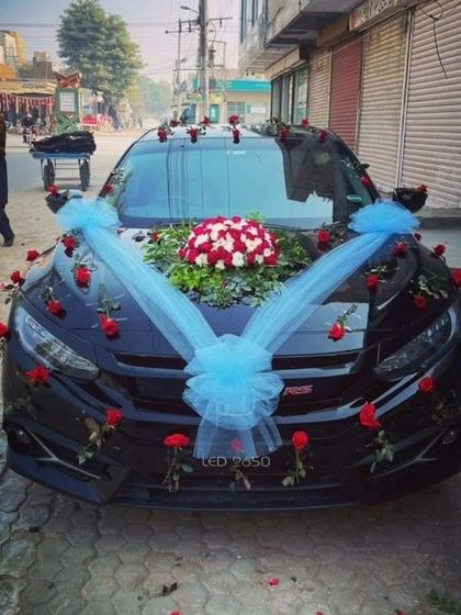 A stylish decoration for a black sedan, using a central floral bouquet with light blue ribbons and scattered red roses.