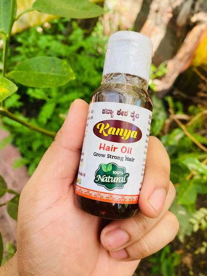 A close-up of the Kanya Hair Oil bottle held in hand, with a natural green background emphasizing its herbal origins.