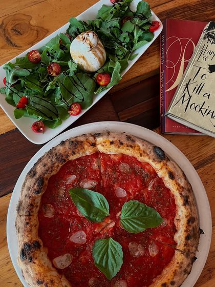 A beautiful spread featuring our Marinara pizza, a burrata salad, and a good book. The perfect solo date.