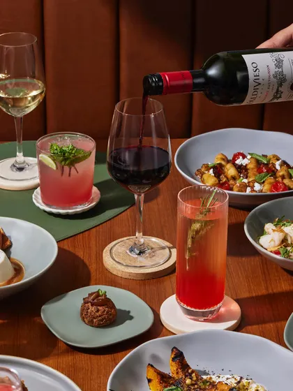 A table full of our signature dishes and drinks. A glass of red wine is poured to accompany plates of gnocchi, panna cotta, and other small bites, perfect for sharing.