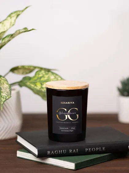 A sophisticated shot of a "Glossy Posse" candle from Kesariya, placed on a stack of books. This styling positions the candle as a chic home decor accessory.