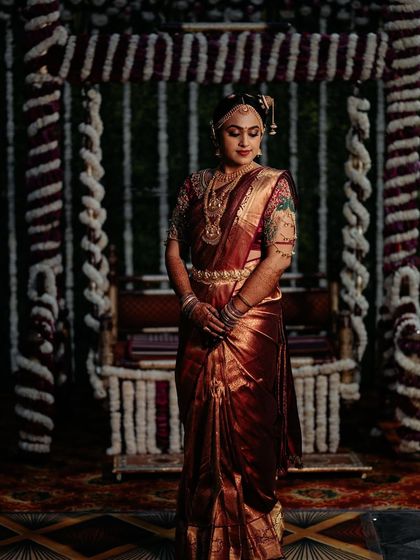 A beautiful bride standing before the Oonjal (swing), an important part of a Tamil wedding. Her maroon silk saree is draped perfectly to showcase its rich zari work.