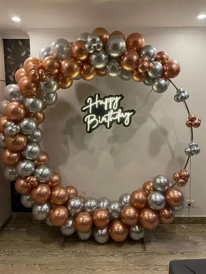 A minimalist yet chic ring backdrop for an adult birthday. The simple metal ring is accented with rose gold and silver chrome balloons, complemented by a "Happy Birthday" neon sign for a modern and understated look.