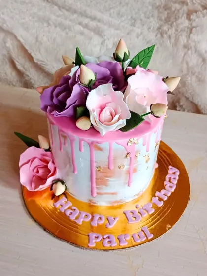 A lovely birthday cake with a pink drip effect over a brushed buttercream base, topped with a bouquet of purple and pink sugar roses.