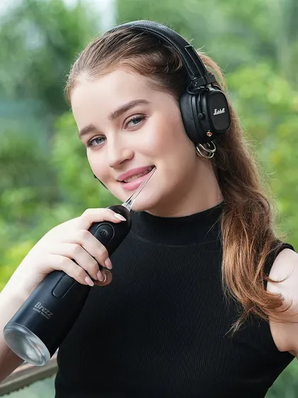A model uses a black water flosser while listening to music. This creative lifestyle shot positions the product as part of a modern, convenient routine.