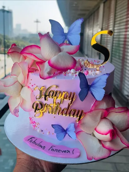 An absolutely beautiful and elegant birthday cake in shades of pink. This design features large, delicate sugar flowers, shimmering gold accents, and graceful butterflies, making it a sophisticated choice for an adult birthday celebration.