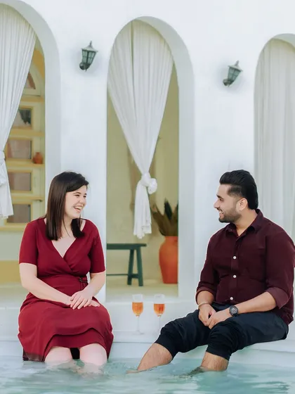 A relaxed and happy moment of a couple enjoying a drink by a Santorini-themed poolside in Jaipur, showing our versatility with different location styles.