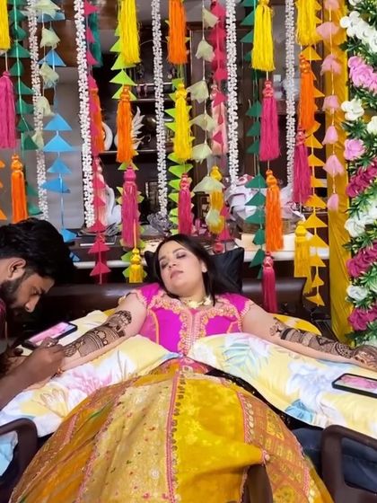 The bride getting her henna done in front of a colorful backdrop of hanging tassels we created for her home Mehandi ceremony.
