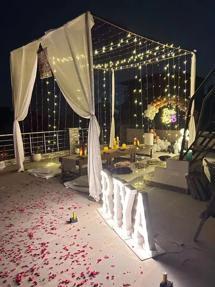 A wider angle of the bachelorette party, showing the full extent of the draped canopy, fairy lights, and seating area on the rooftop.