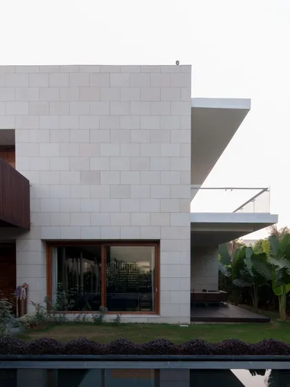 The exterior combines clean lines of modernism with the texture of natural stone cladding. Deep overhangs provide shade and create sheltered outdoor seating areas, blurring the line between the built form and the garden.