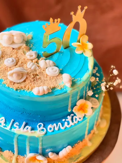 A closer look at the 50th birthday beach-themed cake, showing the detail on the edible sand and handcrafted shells.