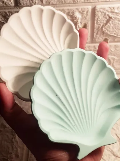 Two of our mini shell dishes in classic white and a soft mint green, held in hand to show their size.