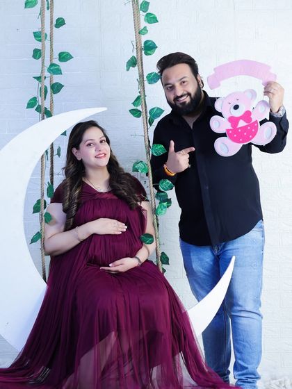 A fun and celebratory couple's shot on our moon swing set. The mom-to-be looks radiant in her gown while her partner playfully points to a "It's a Girl" teddy bear sign.